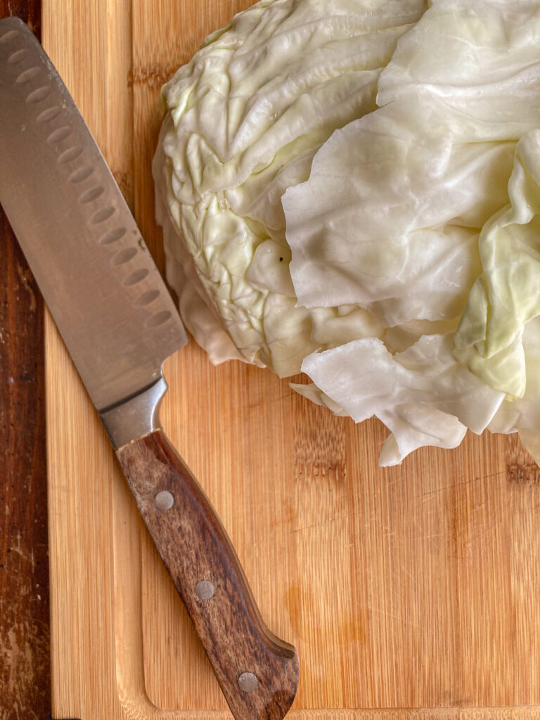 part of  a head of cabbage sitting on a cutting board with a knife