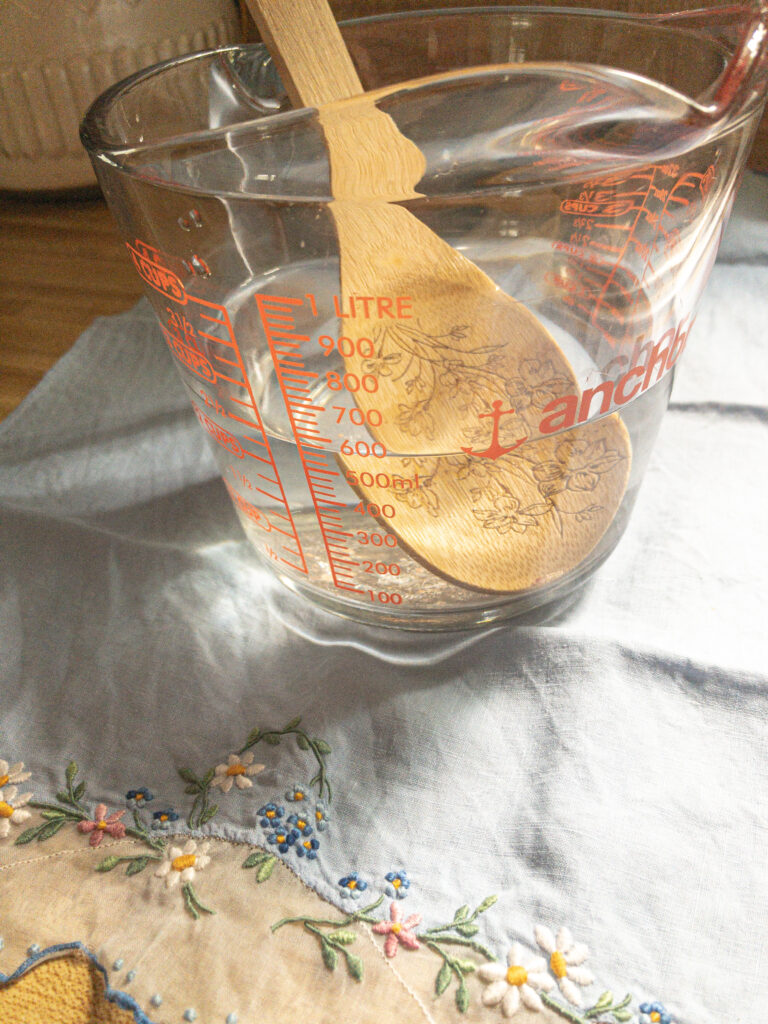 measuring cup of salt and water being stirred with wooden spoon